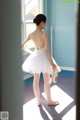 A young ballerina standing in front of a window holding a pair of ballet shoes.