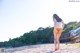 A woman in a white shirt and orange panties walking on a beach.