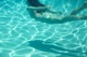 A woman floating in a swimming pool with her shadow on the water.