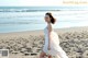 A woman in a white dress is walking on the beach.